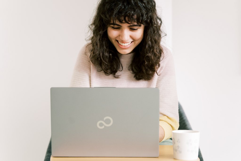 Henkilö istuu tietokoneen ääressä ja hymyilee.