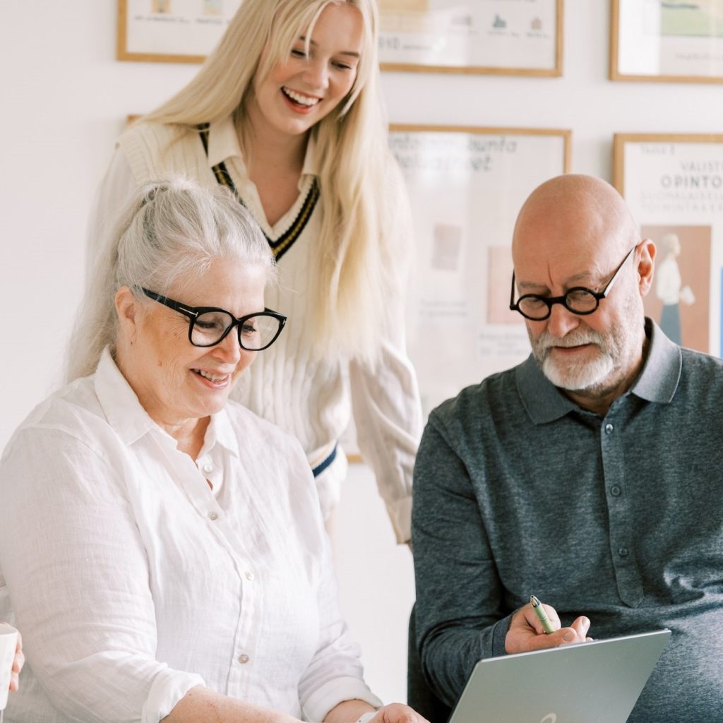 Kolme eri ikäistä henkilöä työskentelee tietokoneen äärellä.