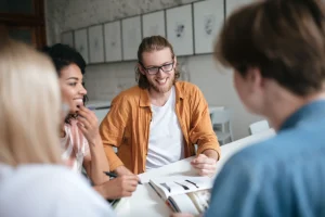 Ryhmäkeskustelutilanne, hymyileviä ihmisiä pöydän äärellä.