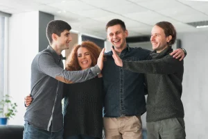 Neljä henkilöä pitää käsiä toistensa olkapäillä ja hymyilee iloisesti.